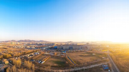 Golden Hour Panorama: An aerial view captures the serene beauty of a town nestled in a landscape of golden fields and rolling hills, bathed in the warm glow of the setting sun.  