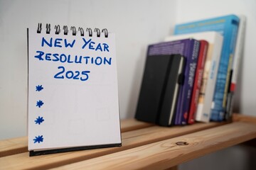 open notebook on a shelf with a sheet of paper with: New Year Resolution and a dotted space for text © siwyk