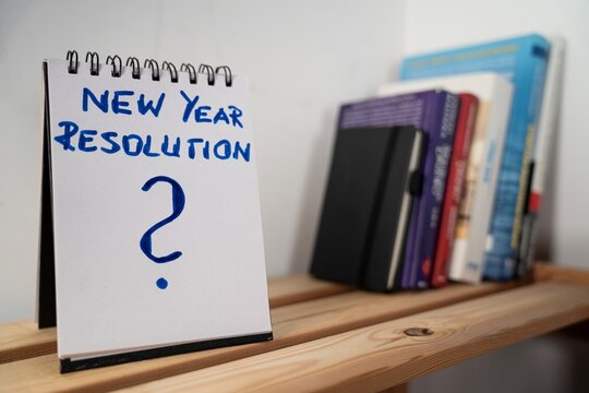 otwarty notes na p&oacute;łce z kartką na kt&oacute;rej zapisany jest: New Year Resolution oraz pytajnik