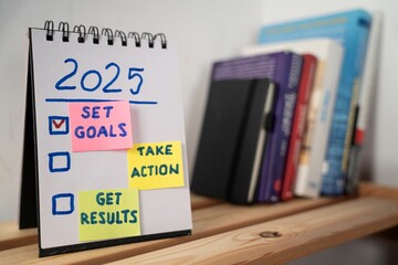otwarty notes na półce z kartką na której zapisany jest 2025 oraz kartki samoprzylepne z napisami: set goals, take action, get results.