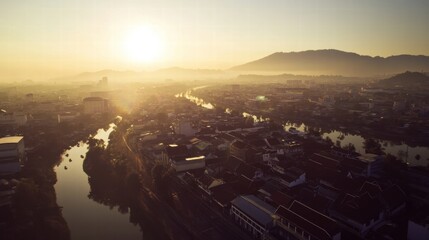 Naklejka premium Golden Hour Cityscape: A breathtaking aerial view captures the ethereal beauty of a city bathed in the warm glow of sunrise. The sun's rays pierce through the morning mist.