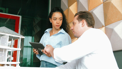 Portrait of project manager pointing at house model while discussion about building design. Caucasian cooperative architect engineer team brainstorming about building material. Teamwork. Manipulator.