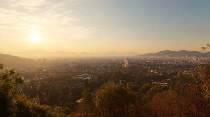 Naklejka premium Golden Hour Panorama: A breathtaking vista of a city bathed in the warm glow of the setting sun, with distant mountains silhouetted against the hazy sky. The scene evokes a sense of peace, serenity.