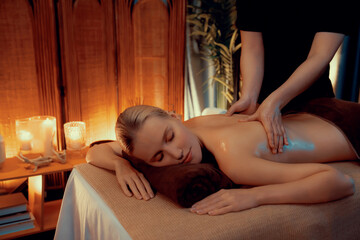Caucasian woman customer enjoying relaxing anti-stress spa massage and pampering with beauty skin recreation leisure in warm candle lighting ambient salon spa at luxury resort or hotel. Quiescent