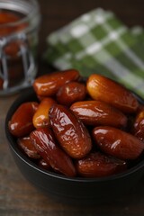 Tasty dried dates in bowl on wooden table, closeup