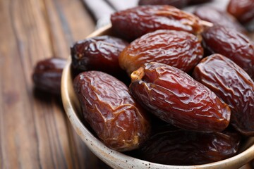 Many tasty dried dates in bowl on brown table, closeup