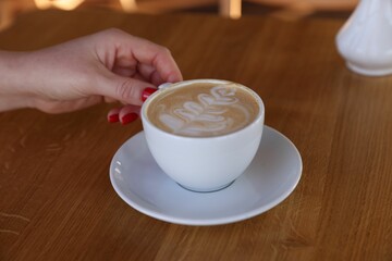 Woman with cup of aromatic coffee at wooden table in cafe, closeup