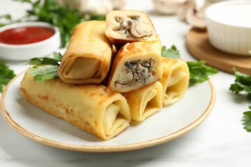 Delicious rolled crepes with mushrooms, parsley, sauce and sour cream on white marble table, closeup