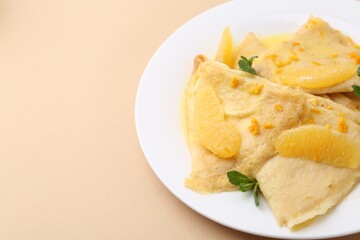 Plate with tasty crepes Suzette on beige table, closeup. Space for text