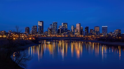 Fototapeta premium A breathtaking cityscape at dusk, skyscrapers glowing with warm golden lights, crisp reflections on a calm river, and a deep, clear blue sky.