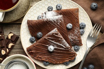 Delicious chocolate crepes with blueberries served on wooden table, flat lay