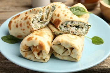 Tasty rolled crepes with cottage cheese and spinach served on wooden table, closeup