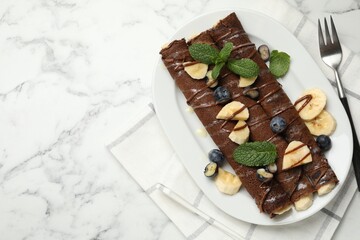 Delicious chocolate crepes with banana and blueberries served on white marble table, top view. Space for text