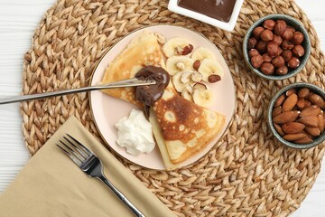Delicious crepes with banana, chocolate paste, whipped cream and nuts on white wooden table, flat lay