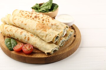 Tasty rolled crepes with cottage cheese and spinach served on white wooden table, closeup. Space for text