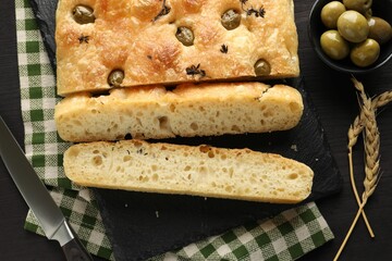 Pieces of delicious focaccia bread with olives, thyme, spikes and knife on dark wooden table, flat lay