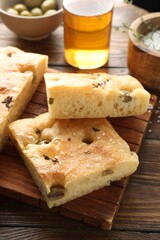 Pieces of delicious focaccia bread with olives, thyme, oil and salt on wooden table, closeup