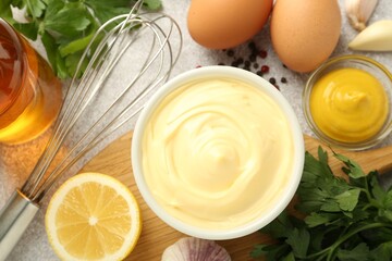 Delicious mayonnaise sauce in bowl, whisk and ingredients on grey table, flat lay