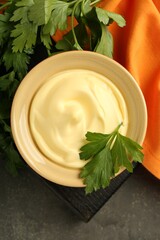 Delicious mayonnaise sauce in bowl with parsley on grey table, top view