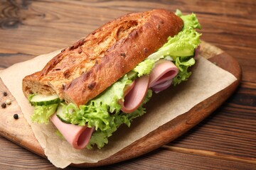 Delicious baguette sandwich with ham on wooden table, closeup