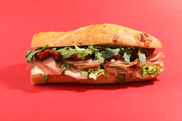 Baguette sandwich with ham and sun dried tomatoes on red background