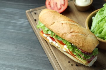 Delicious baguette sandwich with salami and cheese on grey wooden table. Space for text