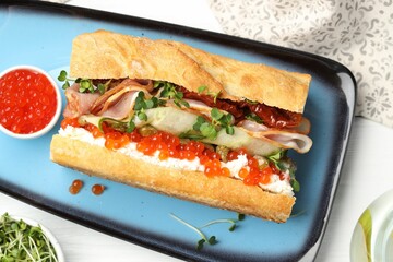 Delicious baguette sandwich with caviar, ham and capers on white wooden table, flat lay
