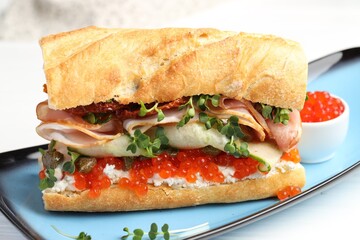 Delicious baguette sandwich with caviar, ham and capers on white wooden table, closeup