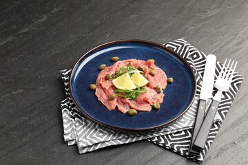 Fresh beef carpaccio with arugula, lemon and capers on dark textured table