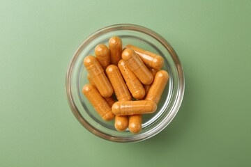 Many turmeric capsules in bowl on light green background, top view