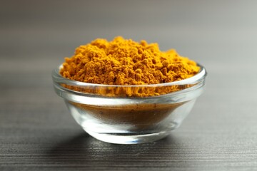 Turmeric powder in glass bowl on grey wooden table, closeup