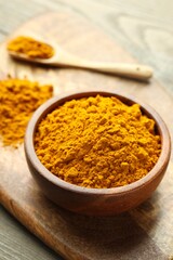 Turmeric powder in bowl on wooden table, closeup