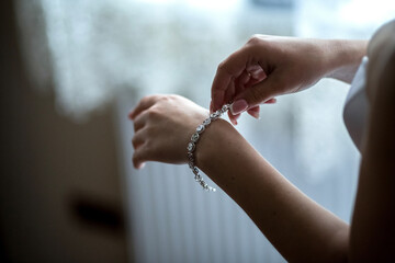 A woman is putting on a bracelet. The bracelet is silver and has diamonds on it. The woman is...