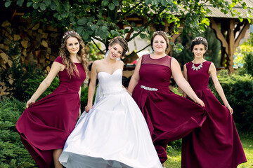 Fototapeta premium Four women in red dresses pose for a picture. One of them is wearing a white dress. Scene is joyful and celebratory, as the women are likely attending a wedding or other special event
