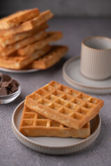 Delicious stacked waffles on plates with crispy texture accompanied by chocolate pieces and elegant cups, perfect for breakfast or brunch inspiration and dessert enthusiasts