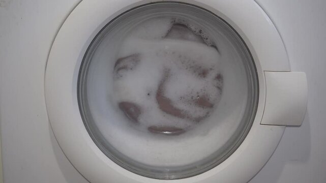 washing clothes in a washing machine, the washing machine is running, the drum of the washing machine is spinning with foam and clothes