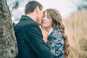 Fototapeta premium A couple is hugging under a tree, with the man kissing the woman's neck. Scene is romantic and intimate