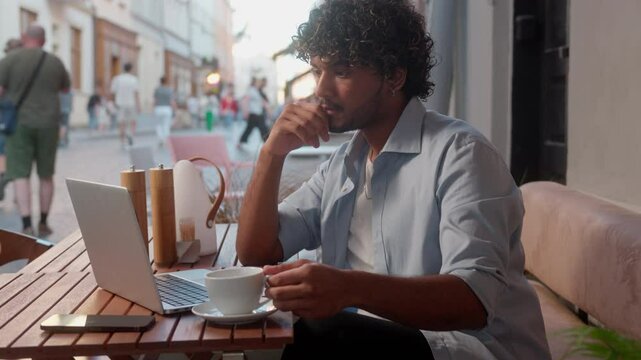 Indian Arabian latino man visitor customer tourist in city cafe drink coffee thoughtful male freelancer business guy student businessman remote working laptop outdoor online studying internet shopping