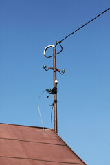 Obraz premium Old rural cottage with improvised electrical connection. Tin roof and metal pole on the rooftop. Traditional style and potential electrical hazard in vintage countryside architecture.