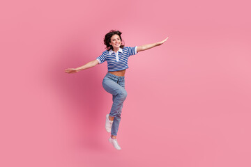 Cheerful woman in striped t-shirt and jeans leaps joyfully against a vibrant pink background,...