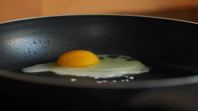 Cracking an egg into a hot frying pan, yolk and white spreading.