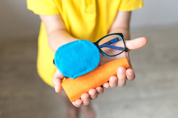 glasses with eye patch with a carrot in boy's hands. Occluder, lazyeye, amblyopia, strabismus. Vision testing concept. Reviewing eyesight