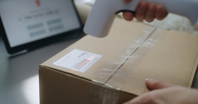 Close Up of Female Shipping and Receiving Clerk Putting Sticker with Track Number on Cardboard Parcel with E-Commerce Order, Scans Code, Preparing for Delivery. Warehouse Facility of Postal Service.
