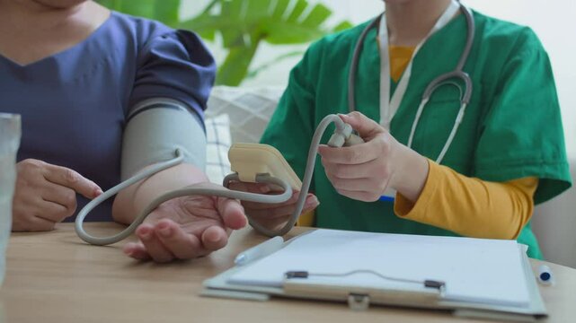 Midsection view of unrecognisable female physician checking blood pressure of unknown senior patient using digital sphygmomanometer and writing down results on clipboard