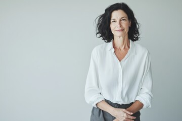 A portrait of a woman with shoulder-length dark hair, wearing a a white shirt with a loose fit against a light grey background.