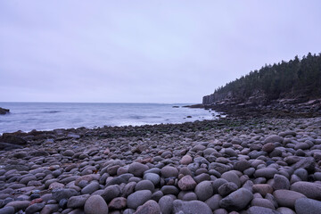 A rocky shoreline covered with large, round, and granite boulders. This area of the Maine coastline is located in Acadia National Park.