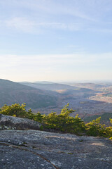 A view from a rocky mountain top in Acadia National Park. The mountains cast shadows on the valley below, and the evergreen shrubery glows green in the sunlight.