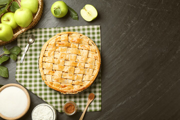 Flat lay composition with tasty homemade apple pie and ingredients on dark textured table. Space...