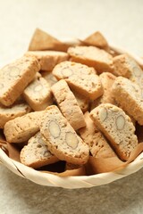 Traditional Italian almond biscuits (Cantucci) in wicker bowl on light textured table, closeup