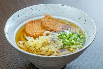A bowl of udon noodles with a clear broth, two pieces of fried tofu, and green onions.